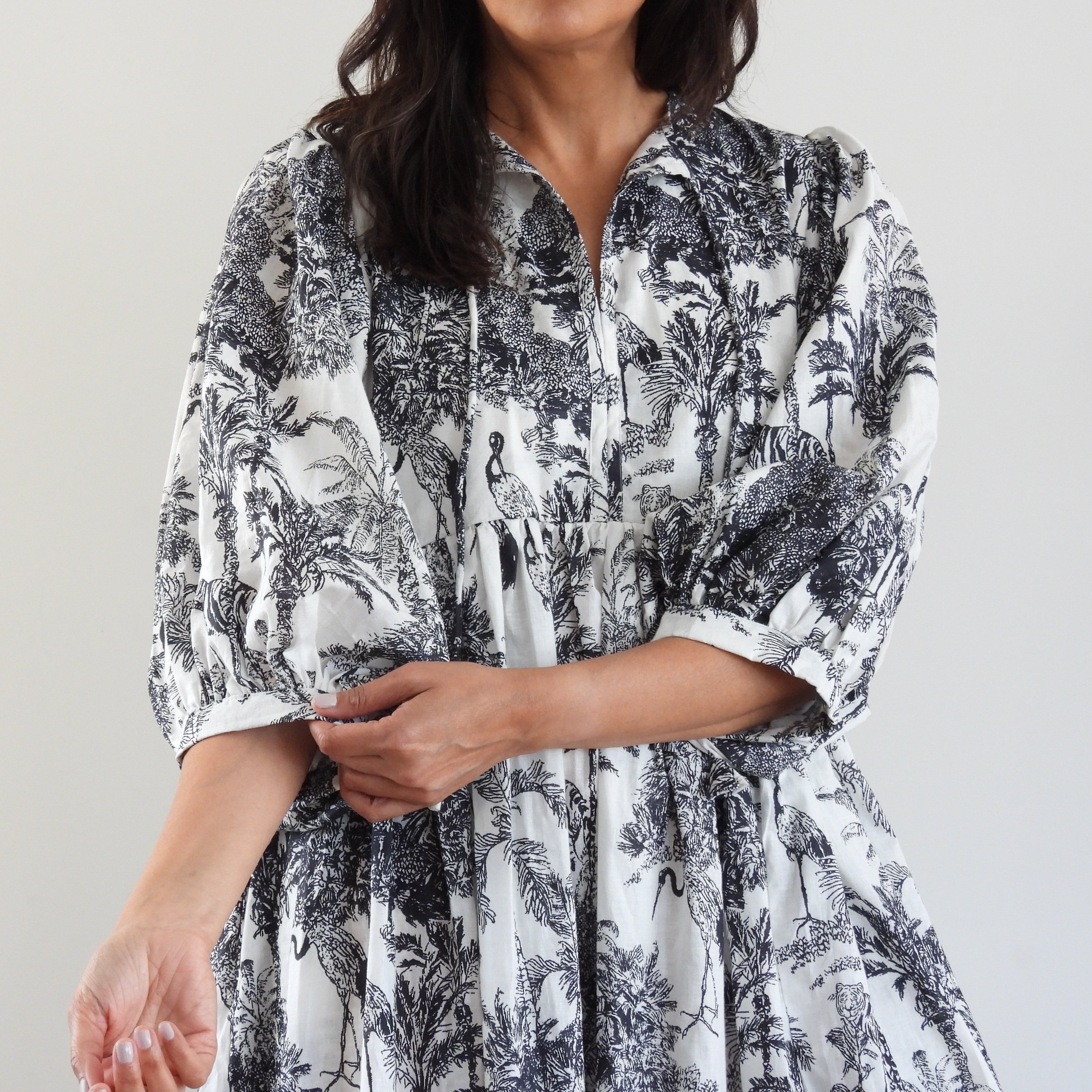 A woman wearing a white and black toile-print dress with three-quarter sleeves and a gathered waist, shown against a plain light gray background.