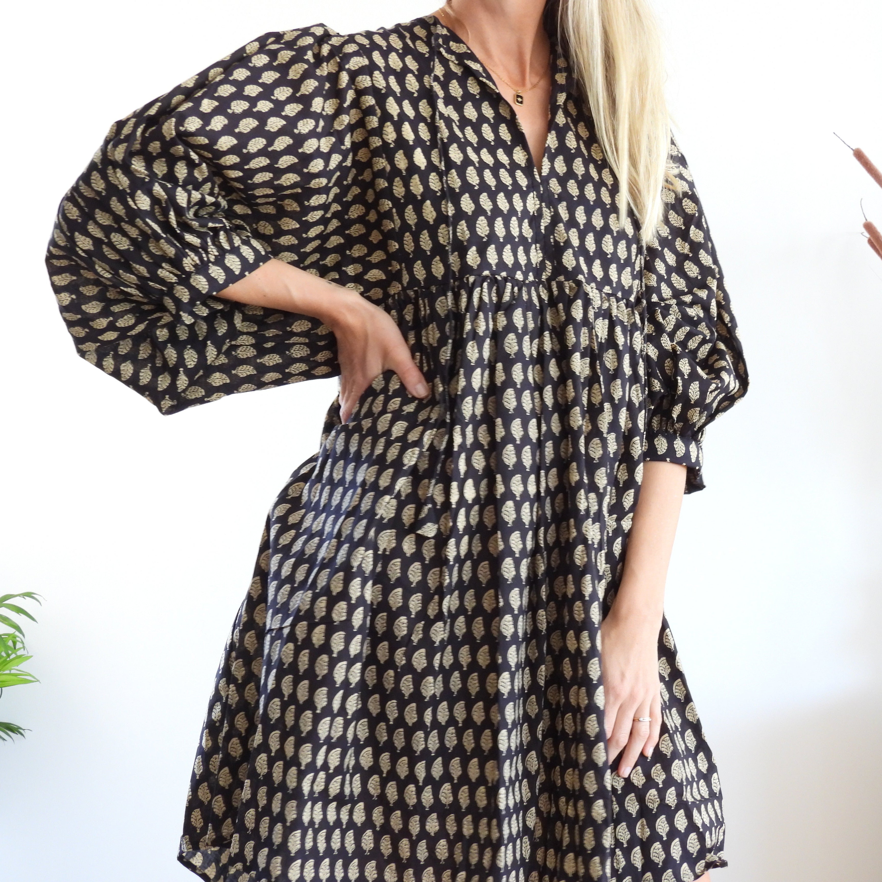 A woman wearing a loose black dress with a beige geometric pattern, featuring voluminous puff sleeves and a split neckline. 