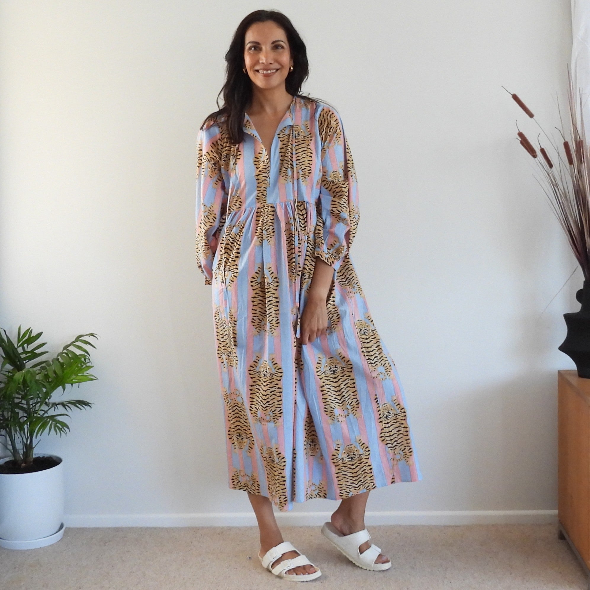 A woman modeling a long-sleeve midi dress with a pink and blue striped base and a brown and gold abstract tiger-like pattern.