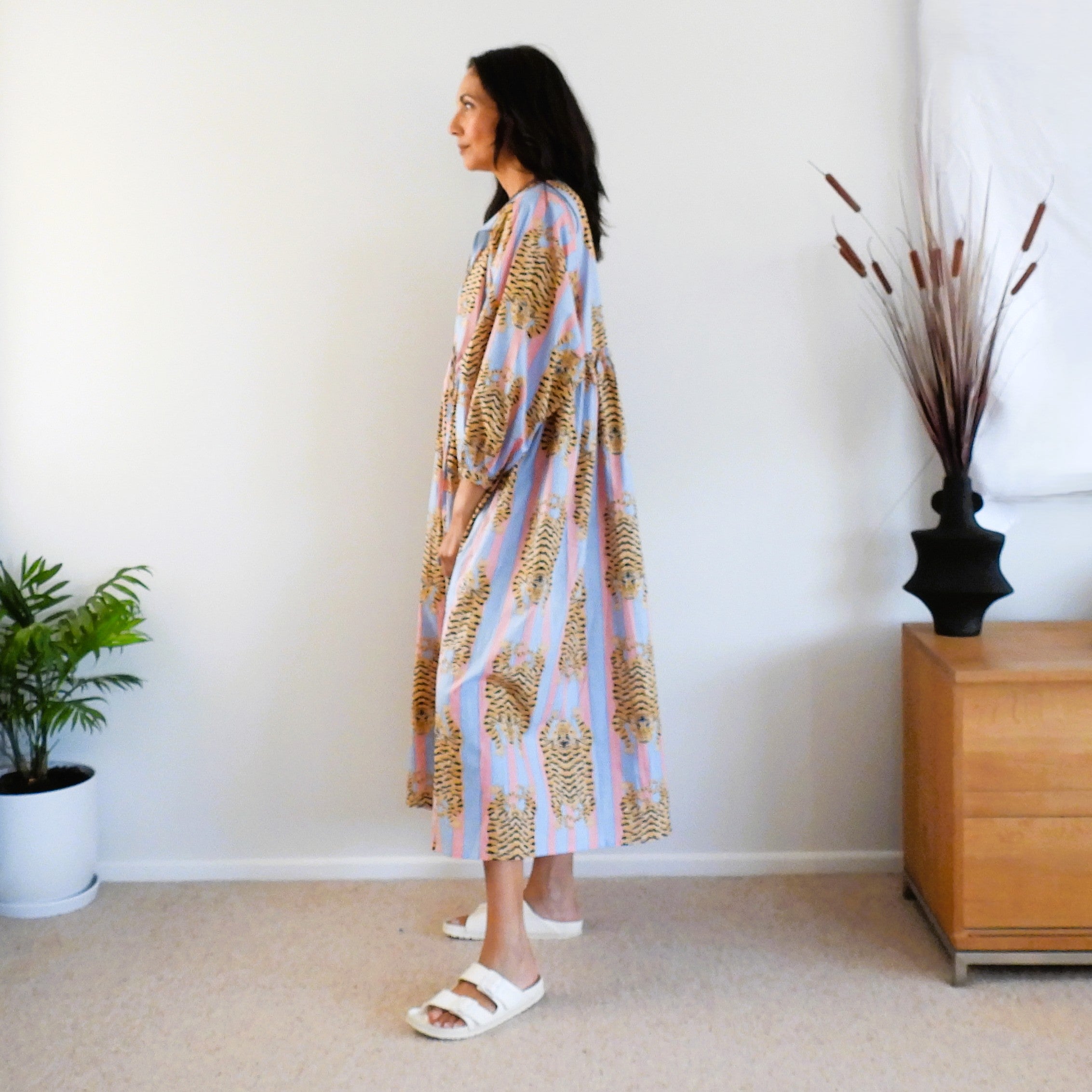 A woman wearing a long, loose kaftan dress with a pastel blue, pink, and gold tiger pattern.
